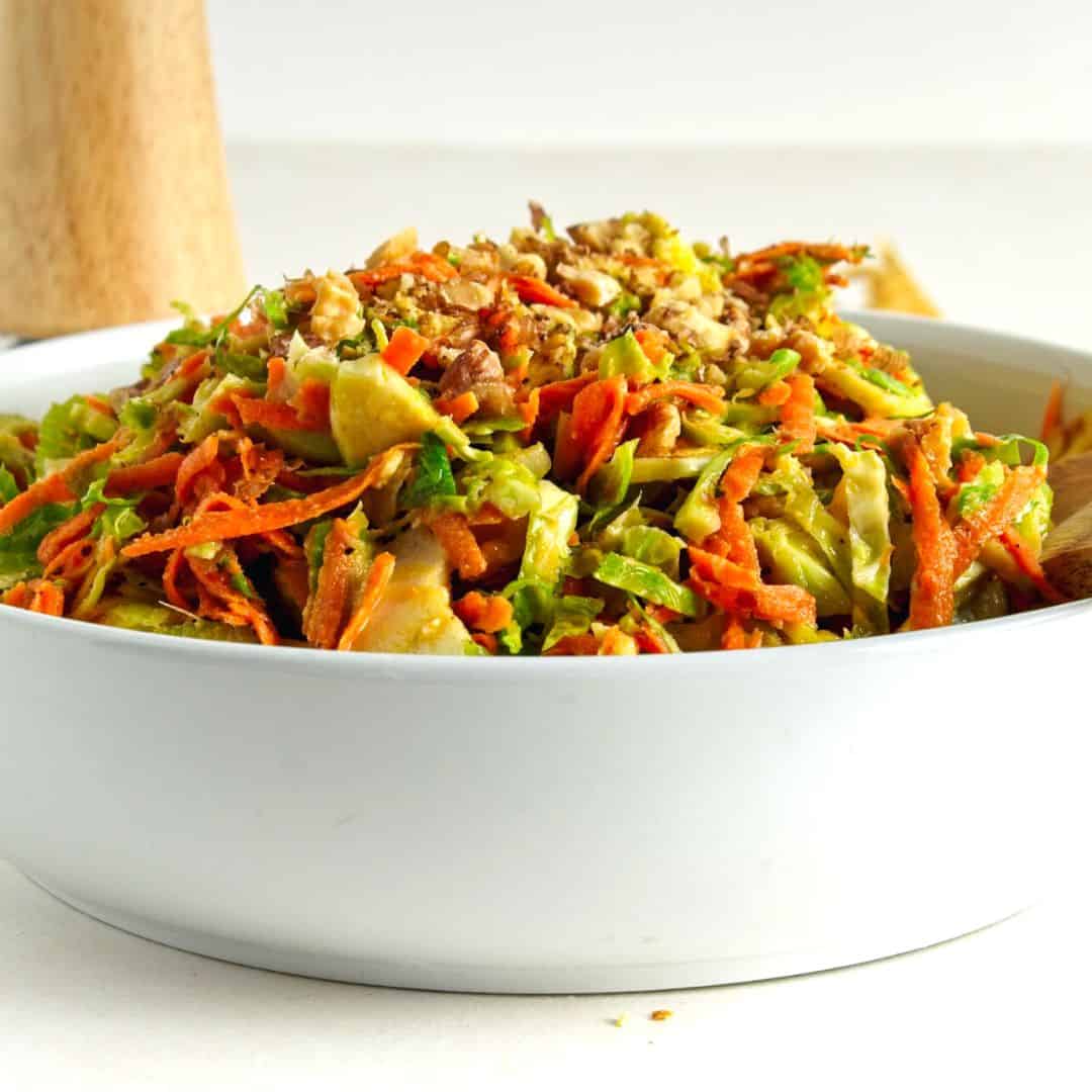 Sweet and Savory Brussels Sprouts Slaw, a simple and delicious vegan recipe made with carrots and apples tossed in a homemade vinaigrette.